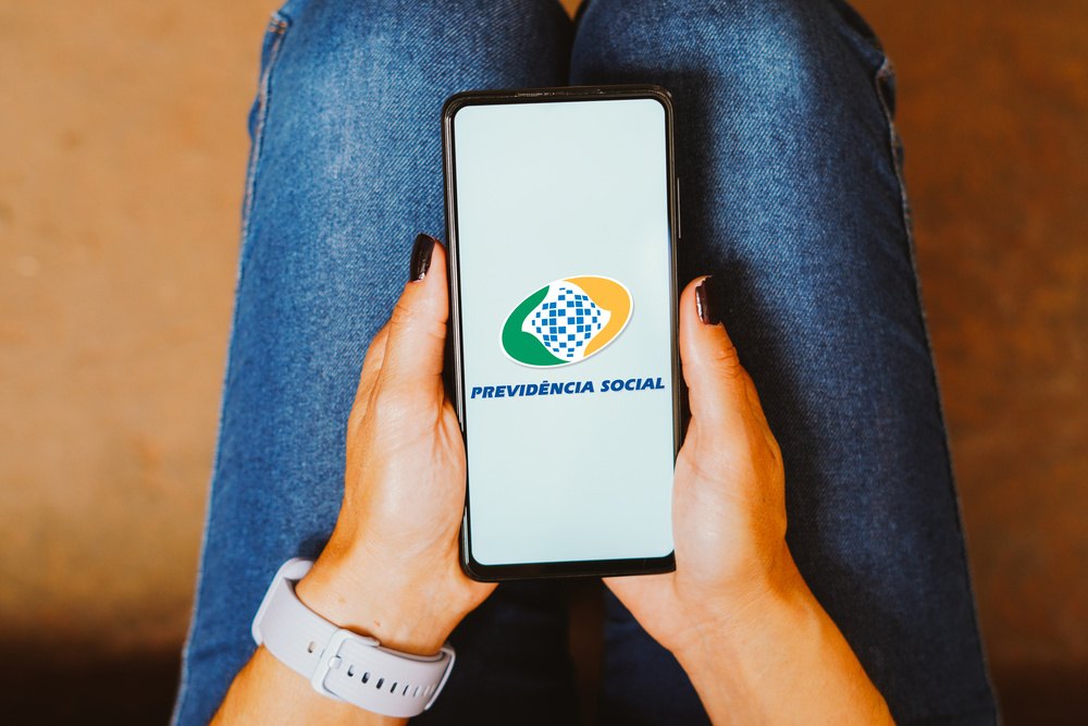 Mulher segurando celular com logo da previdência social