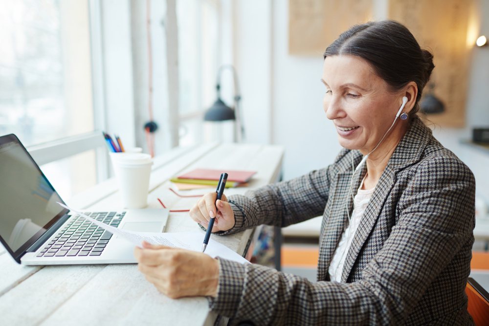 Mulher com folha na mão e Notebook na frente 