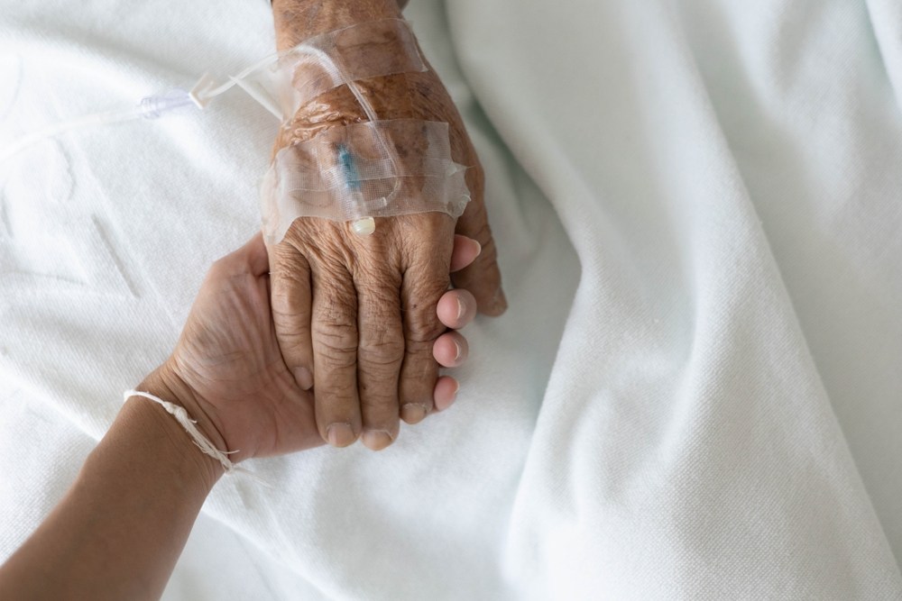 Pessoa jovem segurando mão de uma mulher na 3° idade em uma maca